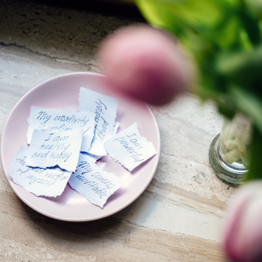 Pink bowl on a table with little papers in them filled with positive affirmations